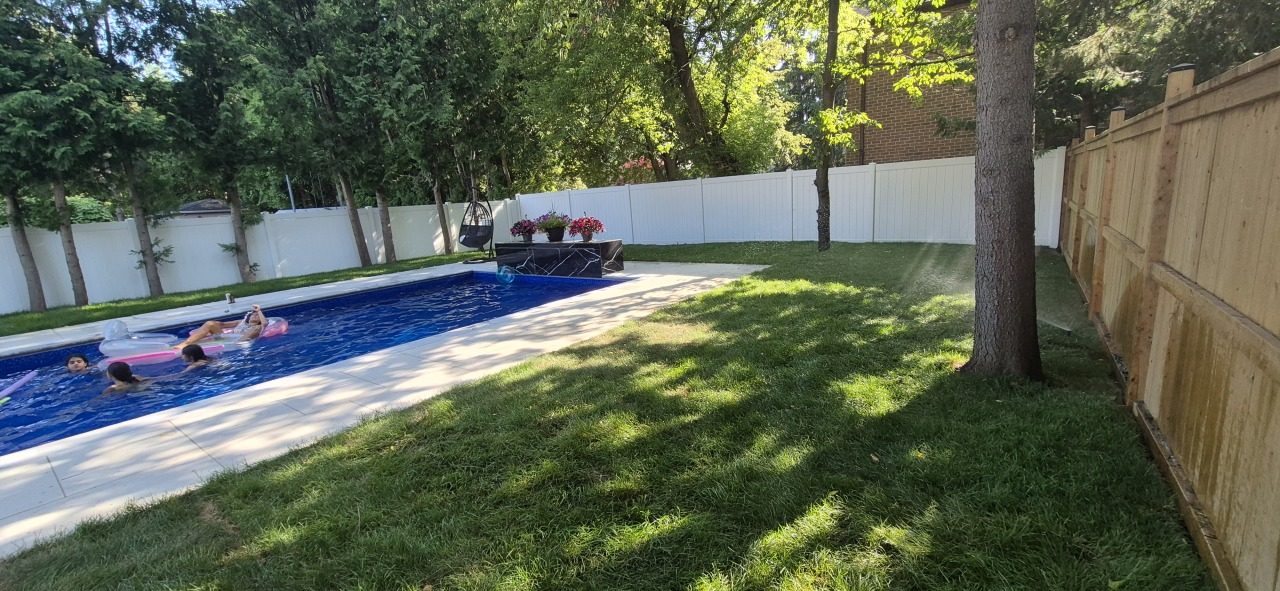 Sprinkler watering a backyard lawn next to a tree, a swing chair and a swimming pool